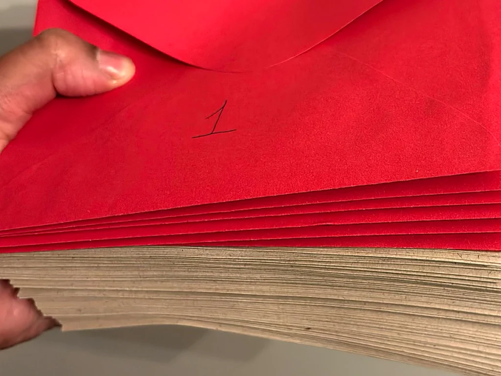「1」と番号が書かれた赤い封筒の束を、手に持っている様子