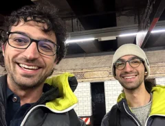 地下鉄のホームで、同じ上着を着た2人の男性が並んで笑っている写真