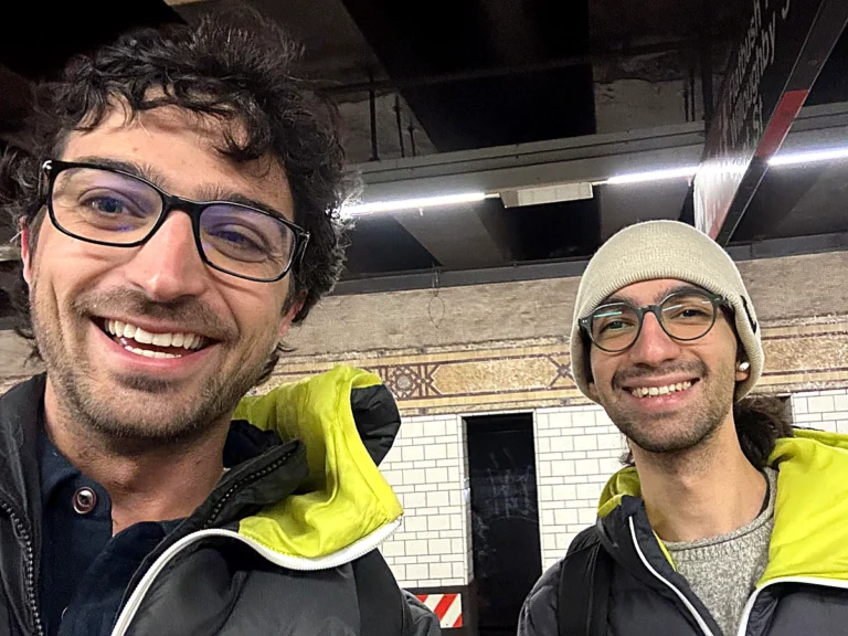 地下鉄のホームで、同じ上着を着た2人の男性が並んで笑っている写真